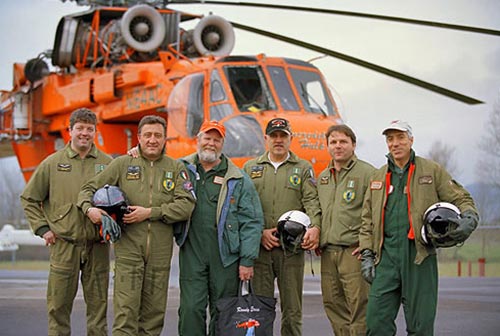 image of 5 men wearing flying uniforms pose in front of a large helicopter