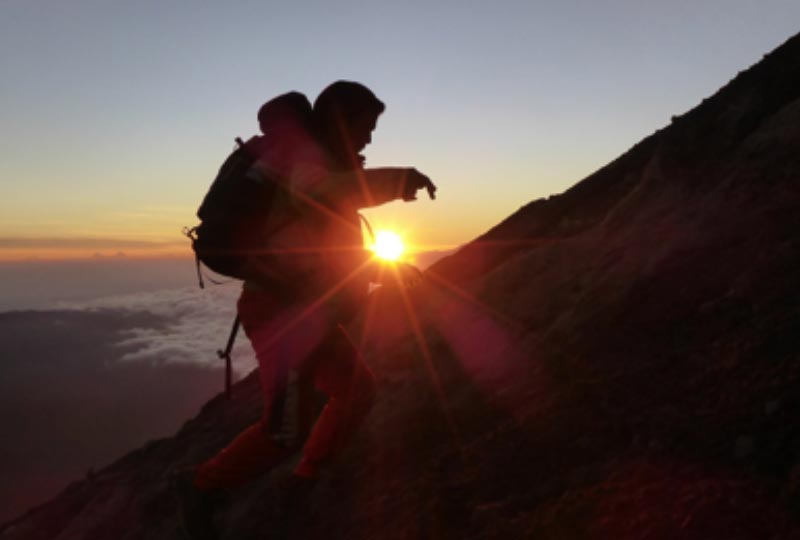 image of a man climbing up the side of a mountain with the sun rising in the background