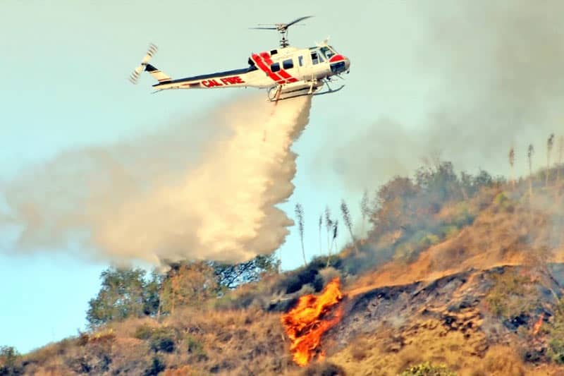image of a helicopter dumping water onto a fire on the hill below