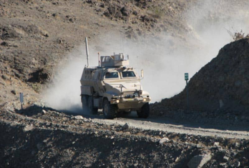 a large, tan off road vehicle driving through rough terrain