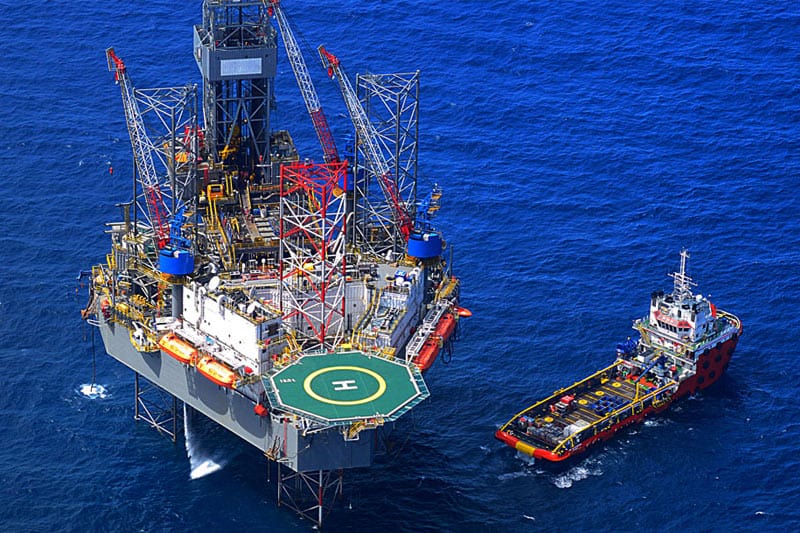 image of an oil platform in the ocean with a red ship next to it